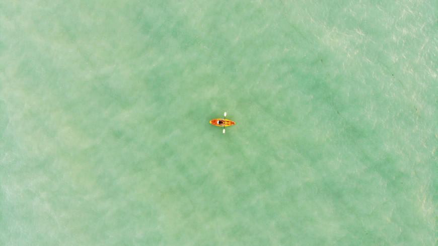 Kuvassa on vihreällä merellä soutava yksinäinen soutuvene. Kuva on otettu ilmasta käsin.