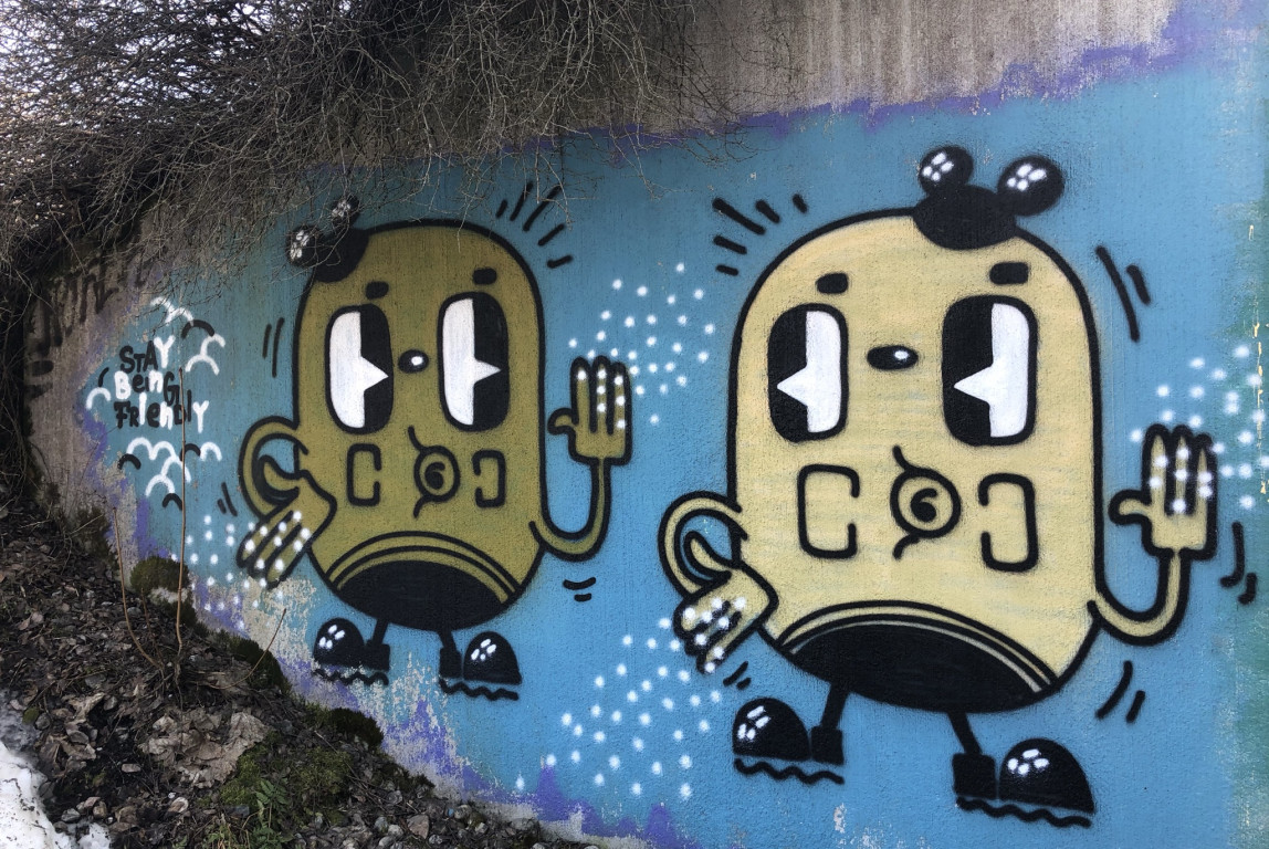 Kuvassa graffitikuva, jossa kaksi perunanmallista hahmoa heiluttelee toisilleen, kuva on koristeellinen.