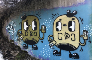 Kuvassa graffitikuva, jossa kaksi perunanmallista hahmoa heiluttelee toisilleen, kuva on koristeellinen.