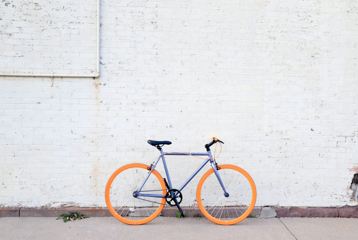 Kuvassa sininen polkupyörä nojaa harmaata seinää vasten.