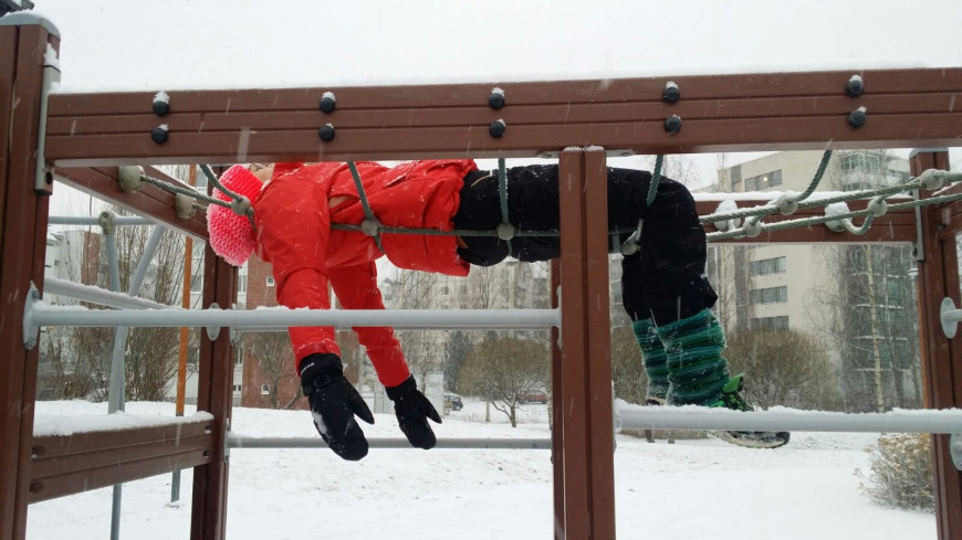 Kuvassa ihminen makaa selällään raajat roikkuen lasten kiipeilytelineessä lumisateessa.